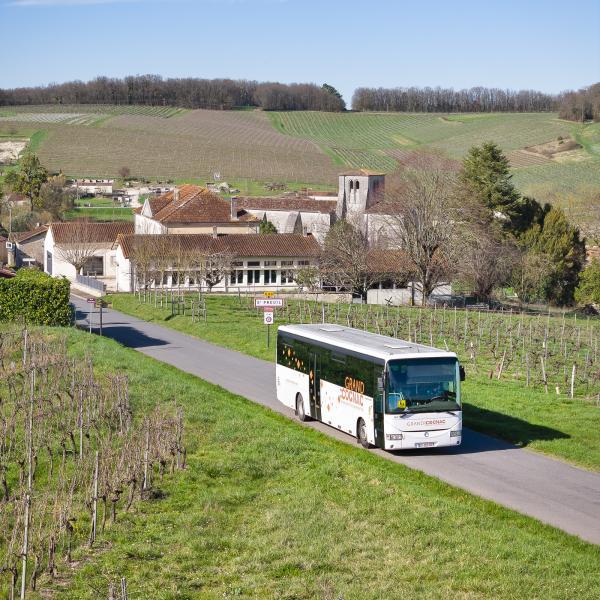 Photo d'un bus scolaire floqué Grand Cognac prise au drone. Le car circule sur une route de campagne en sortie de village.