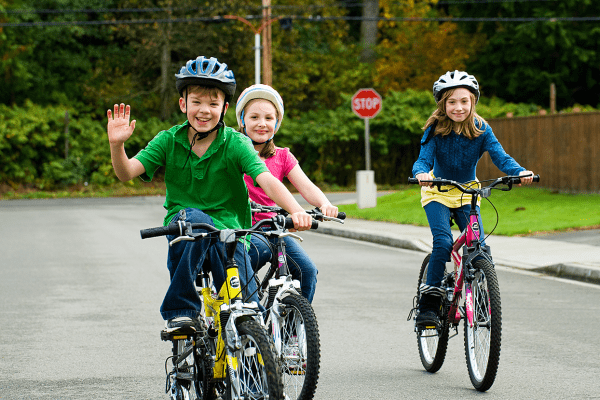 Des enfants à vélo, qui saluent, ils ont un casque. 