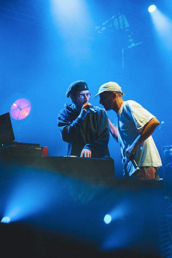 Photo de deux rappeurs face à face, lumière tamisée bleue et micro à la main